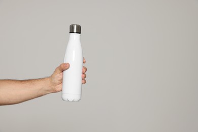 Man holding thermo bottle on light grey background, closeup. Space for text