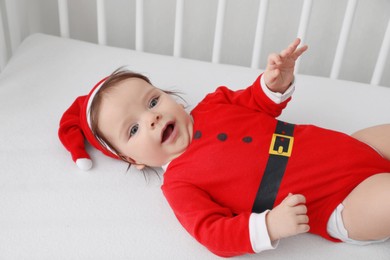 Cute baby wearing festive Christmas costume lying in crib