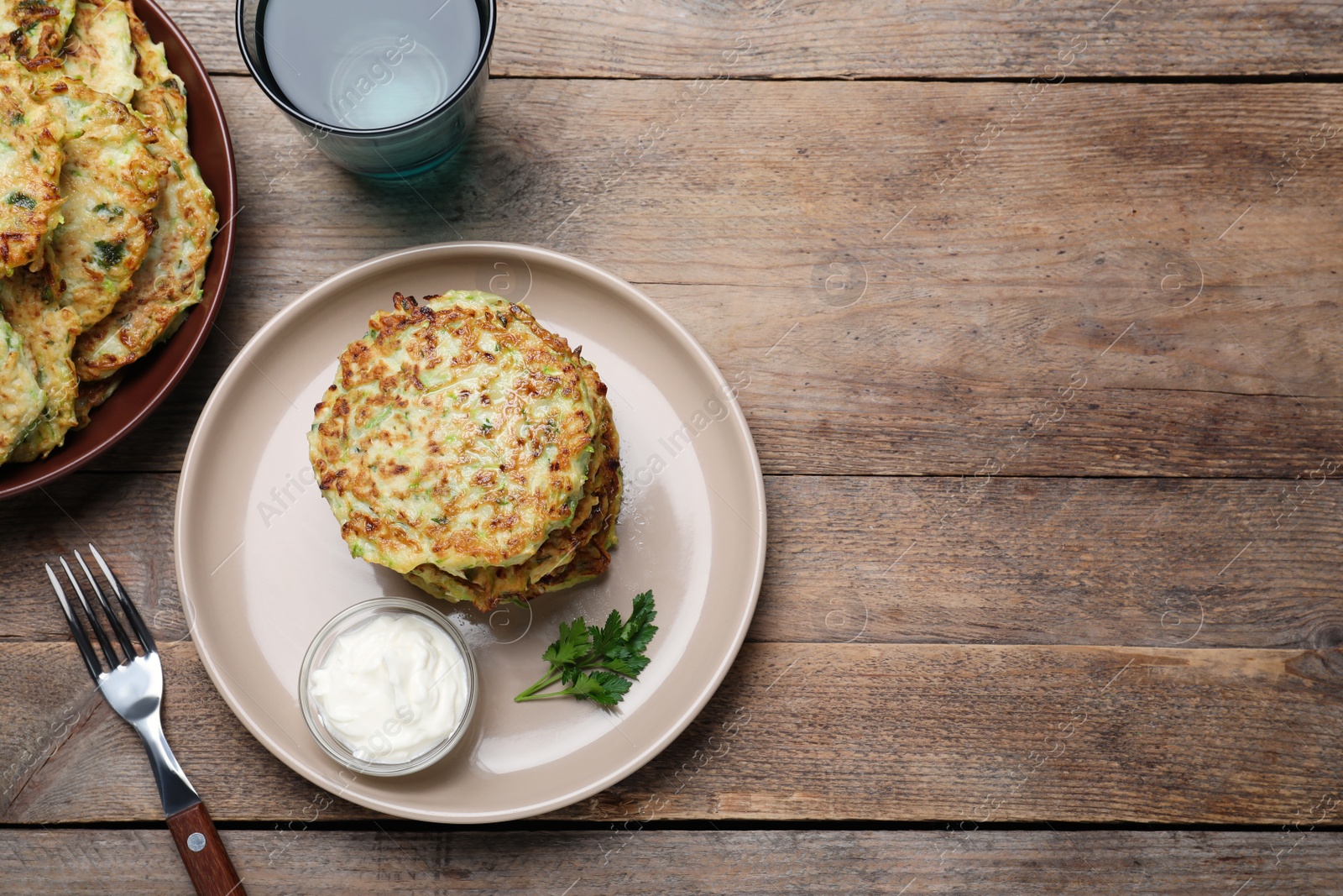 Photo of Delicious zucchini fritters with sour cream served on wooden table, flat lay. space for text