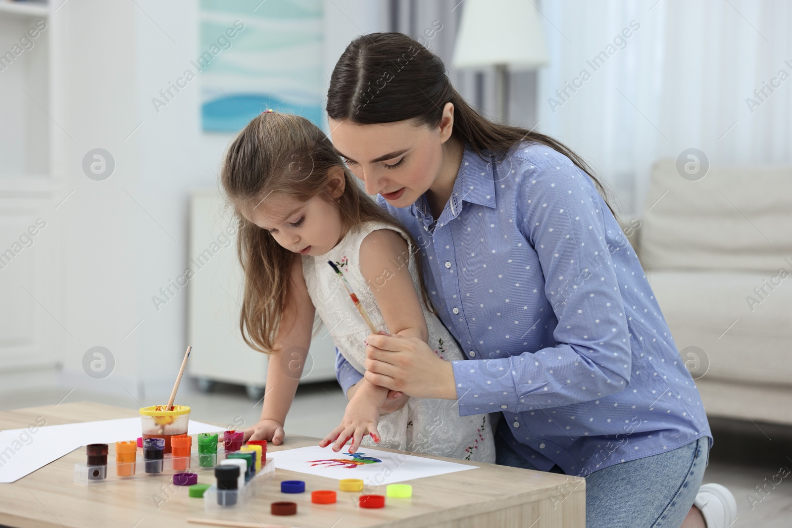 Photo of Mother and her little daughter painting with palms at home