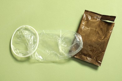 Unrolled female condom and torn package on light green background, above view. Safe sex