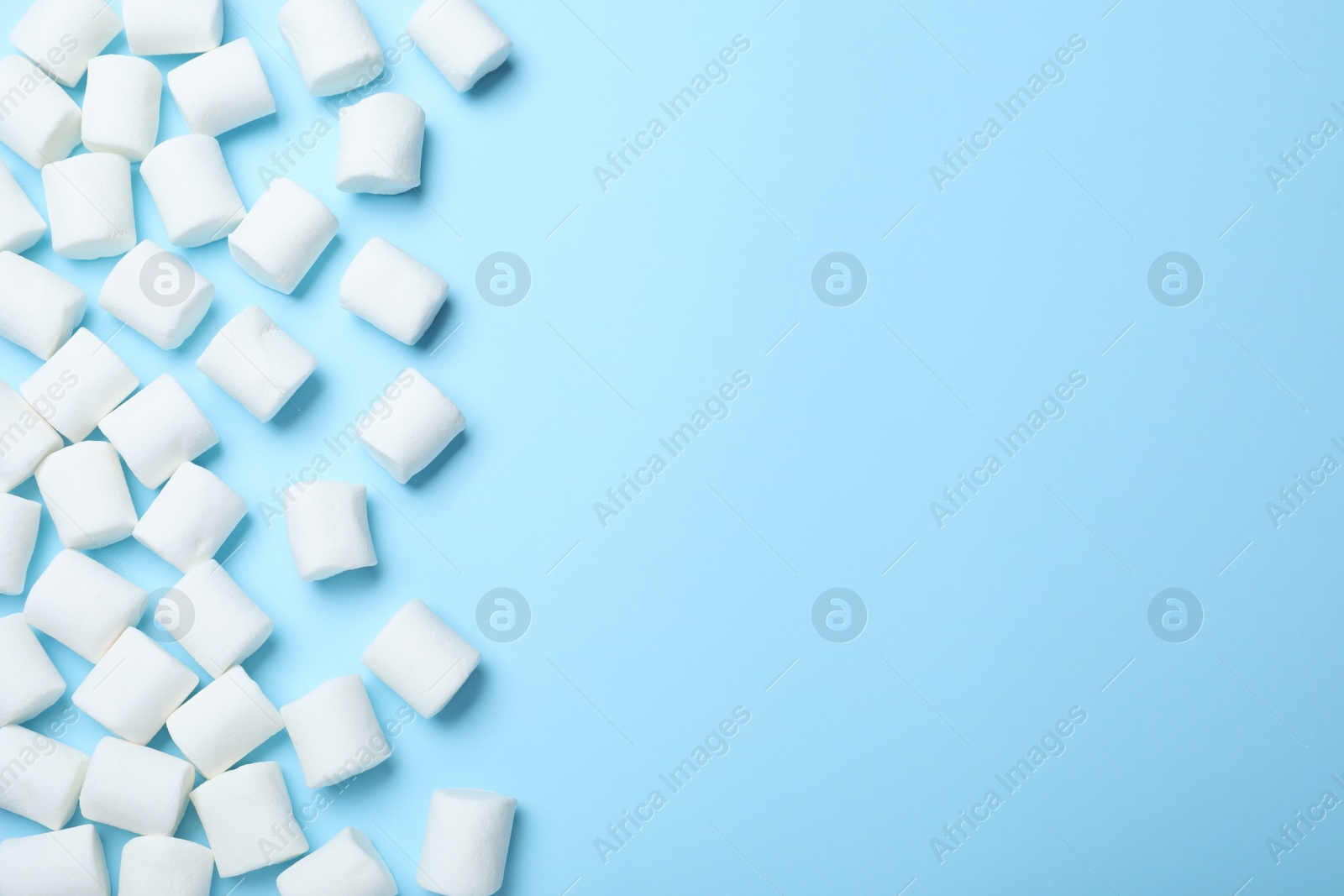 Photo of Delicious puffy marshmallows on light blue background, flat lay. Space for text