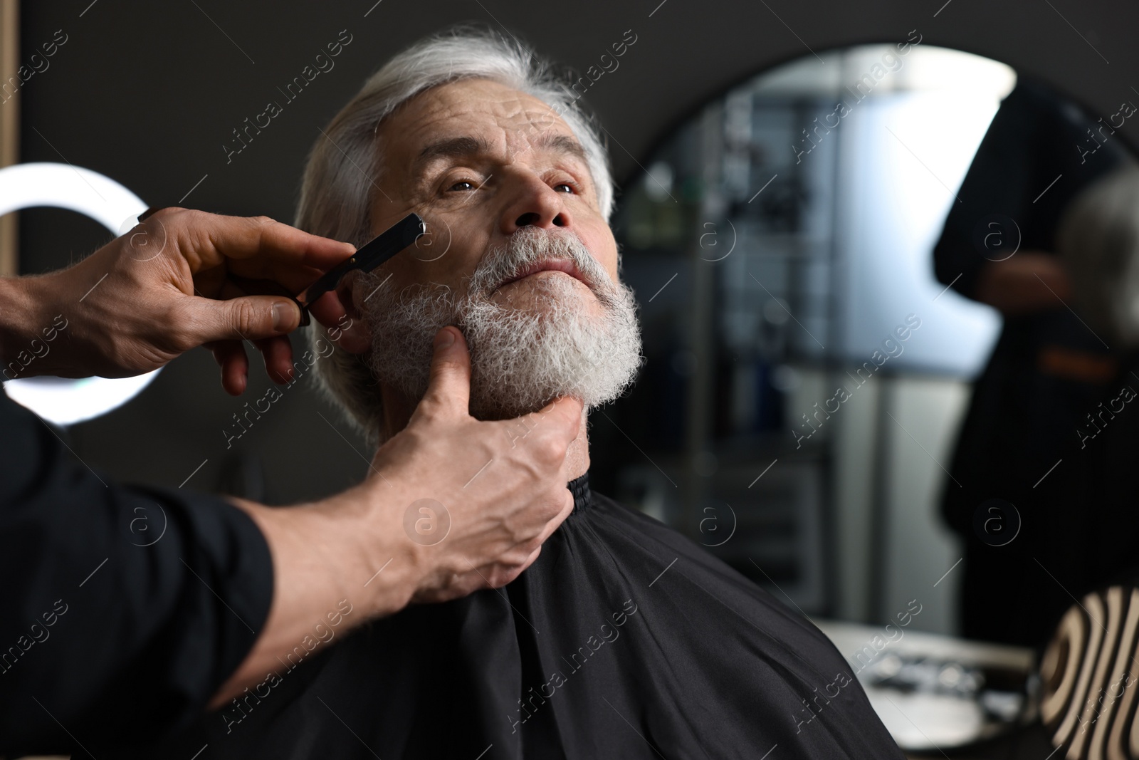 Photo of Professional barber shaving client's beard with blade in barbershop, space for text