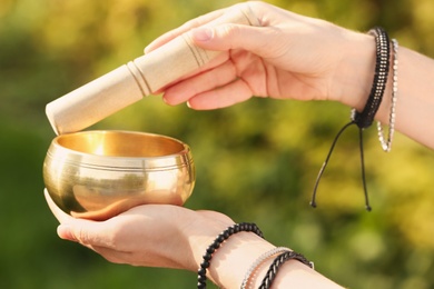 Photo of Woman using singing bowl in sound healing therapy outdoors, closeup