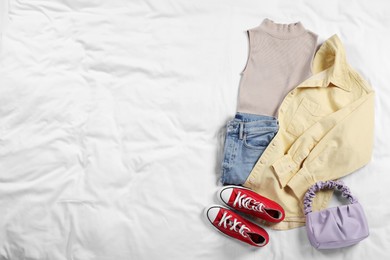 Photo of Pair of stylish red sneakers, clothes and bag on white fabric, flat lay. Space for text