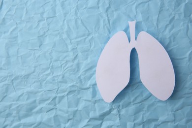 Photo of Paper in shape of human lungs on light blue crumpled background, top view. Space for text