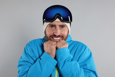 Photo of Winter sports. Happy man in ski suit and goggles on gray background