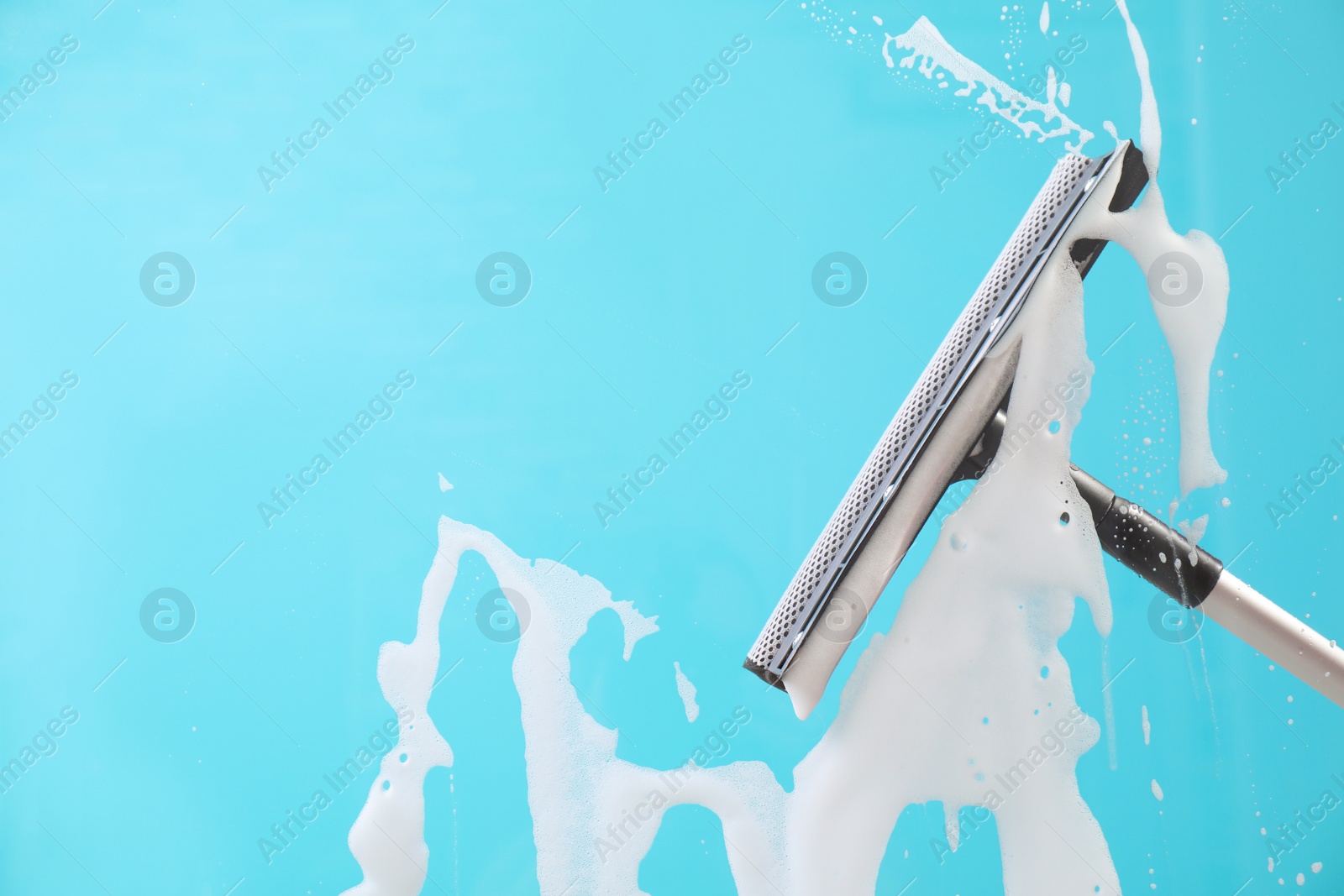 Photo of Cleaning glass with squeegee on color background