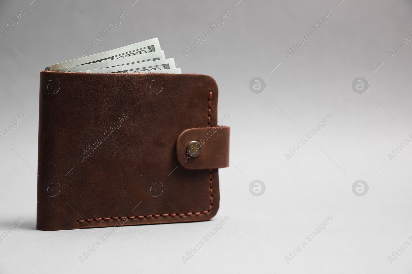 Photo of Stylish brown leather wallet with dollar banknotes on light grey background. Space for text