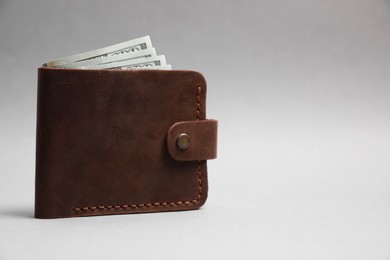 Stylish brown leather wallet with dollar banknotes on light grey background. Space for text