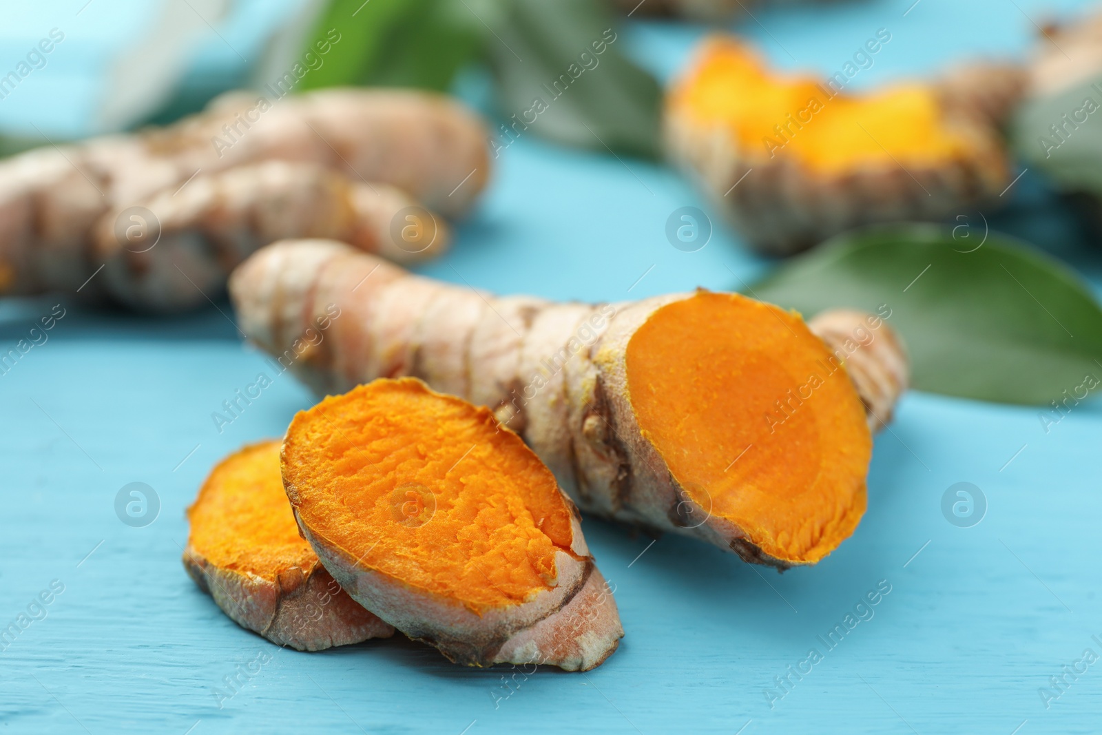 Photo of Cut turmeric roots on light blue wooden table, closeup