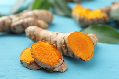 Photo of Cut turmeric roots on light blue wooden table, closeup