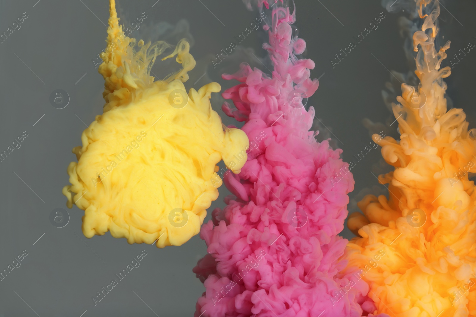 Photo of Splash of pink, yellow and orange inks on grey background