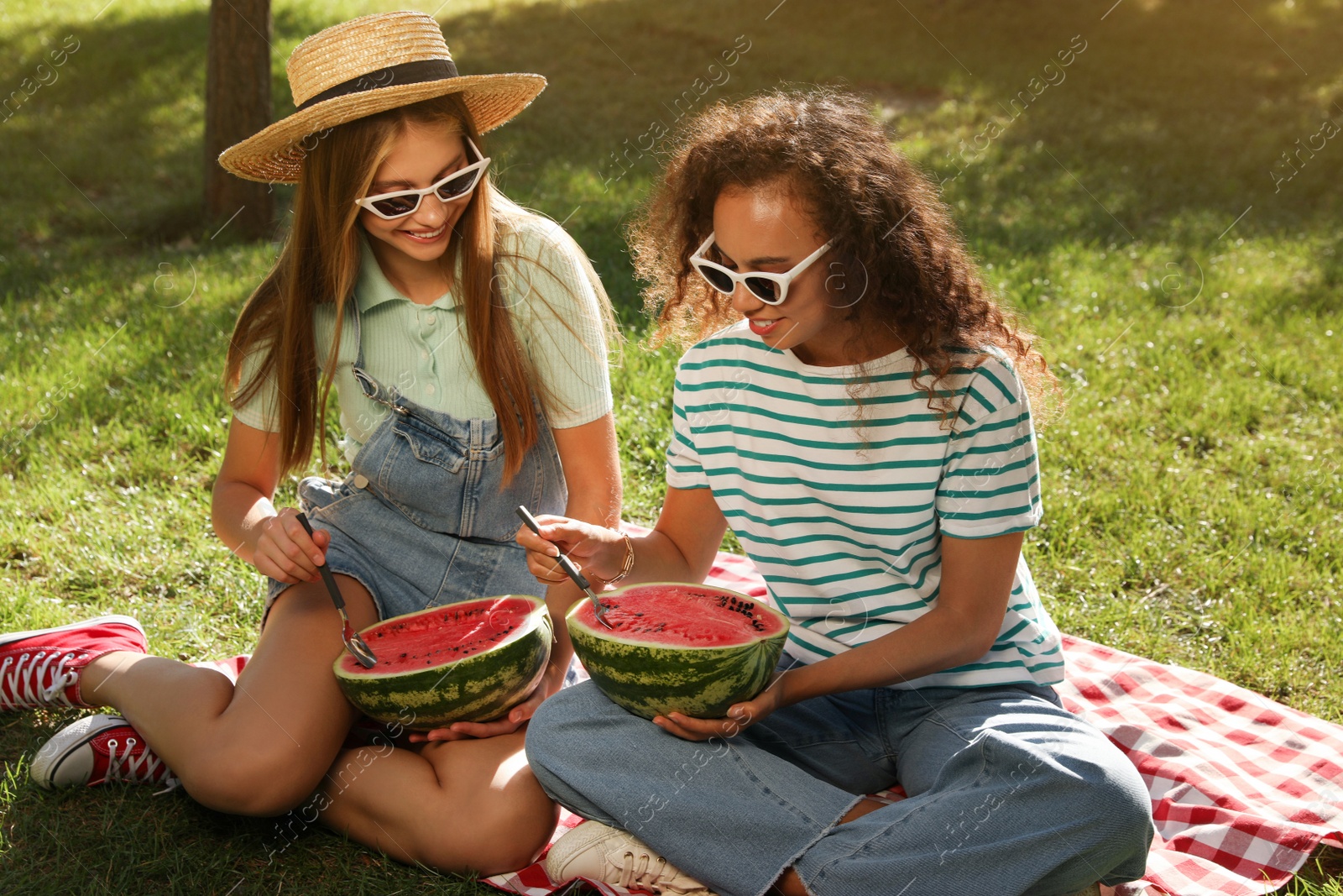 Photo of Happy girls eating watermelon on picnic blanket in park