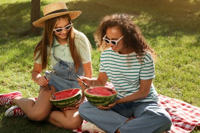 Happy girls eating watermelon on picnic blanket in park