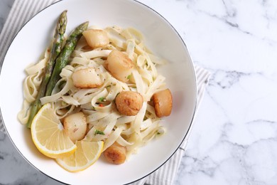 Photo of Delicious scallop pasta with asparagus and lemon on white marble table, top view. Space for text