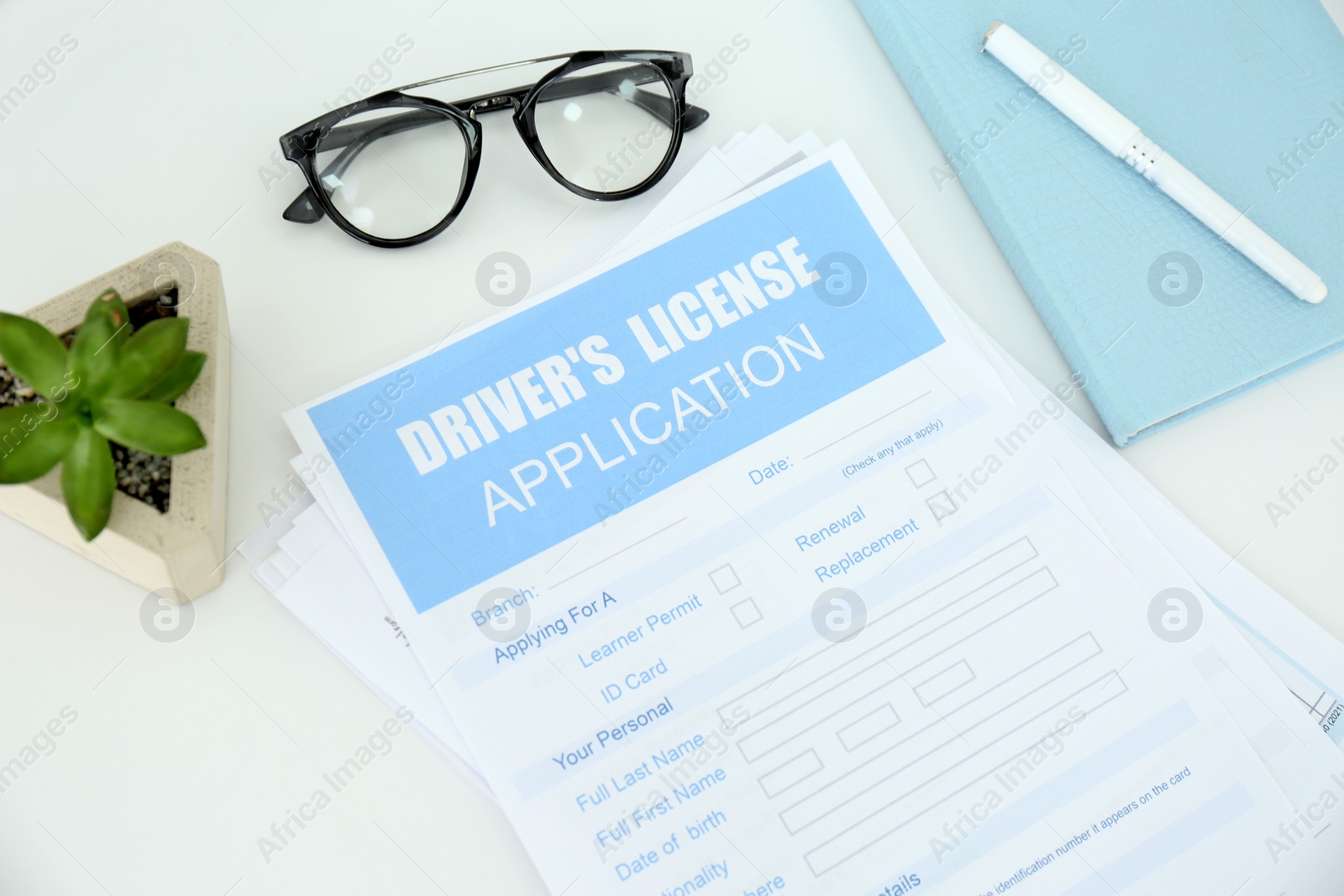 Photo of Driver's license application form with stationery, glasses and plant on white table
