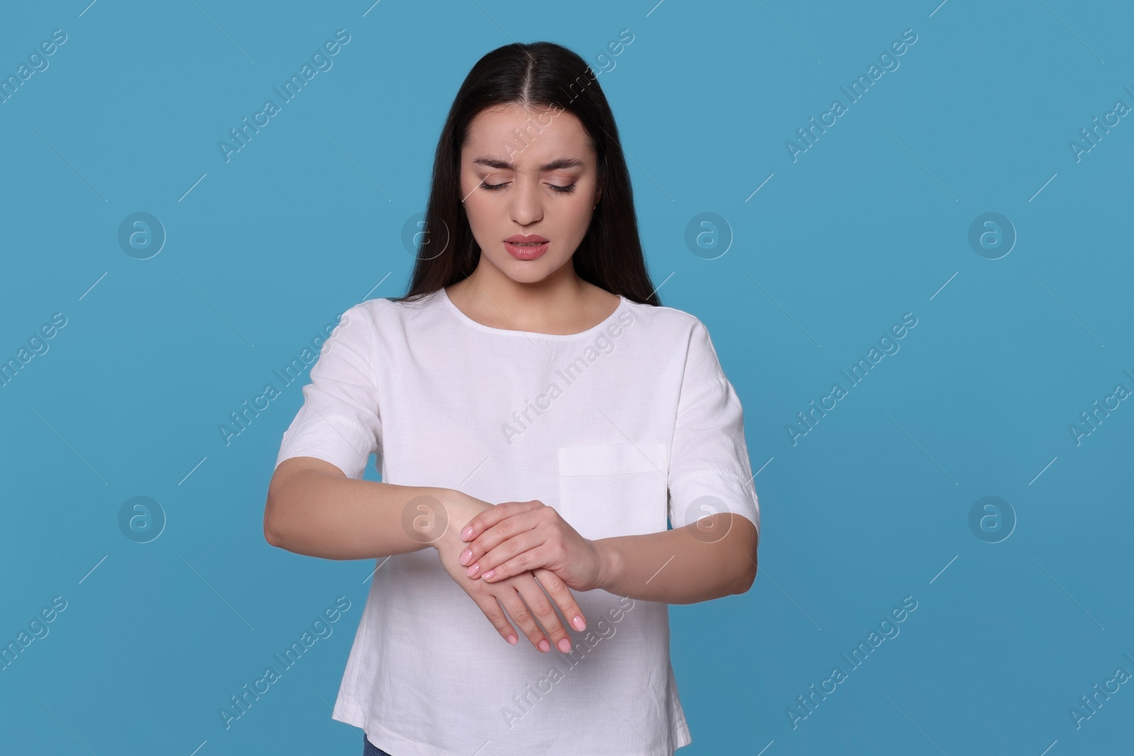 Photo of Young woman suffering from pain in hands on light blue background. Arthritis symptoms