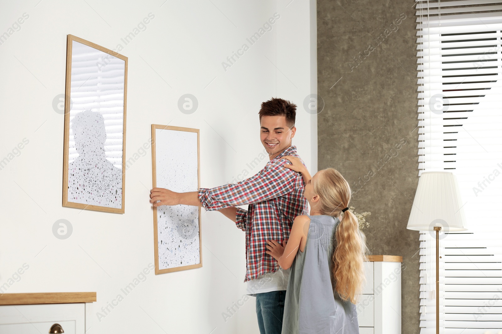 Photo of Father and daughter hanging picture on wall at home