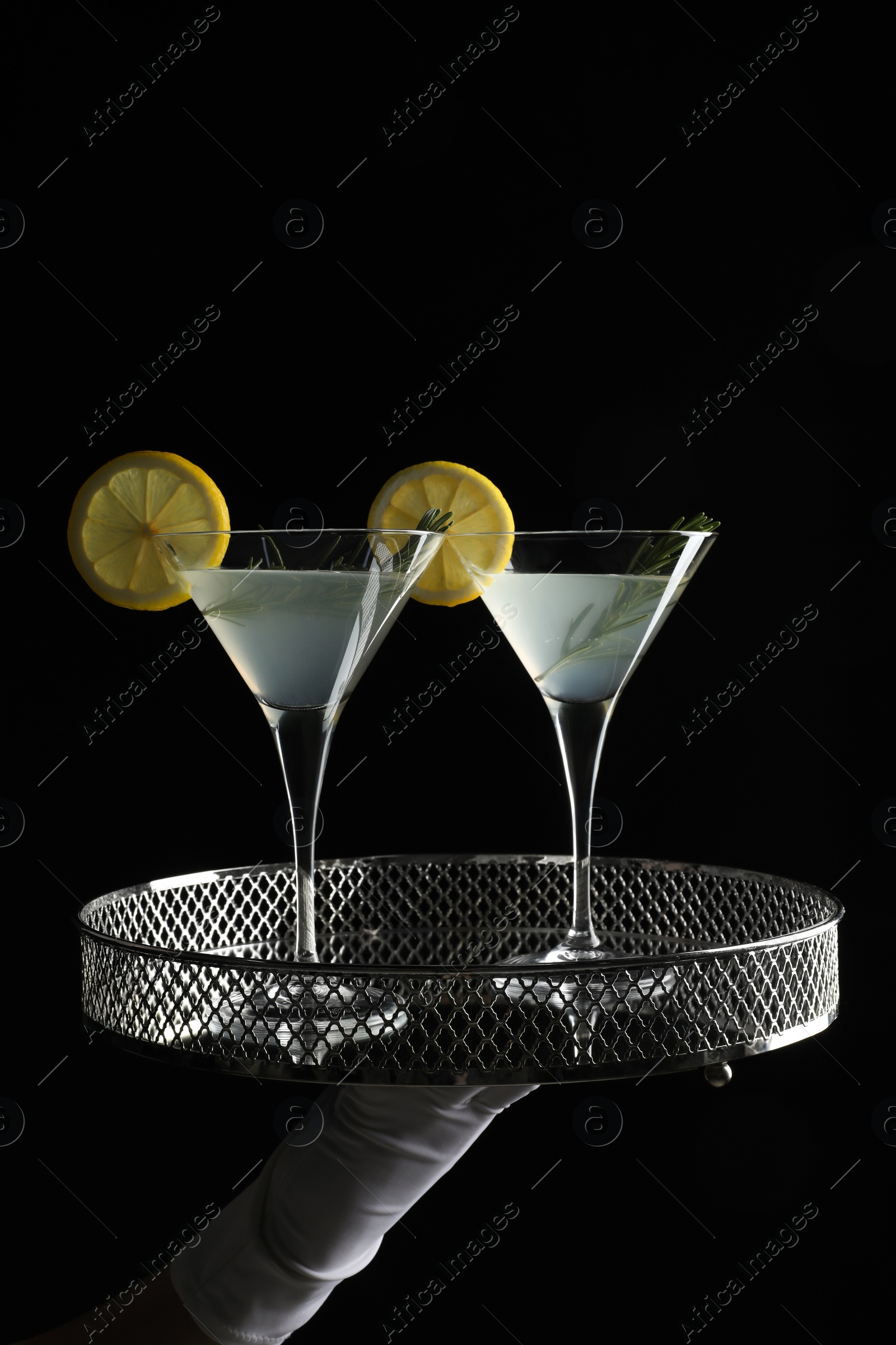 Photo of Waiter holding elegant tray with martini glasses of fresh cocktail against black background, closeup