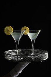 Waiter holding elegant tray with martini glasses of fresh cocktail against black background, closeup
