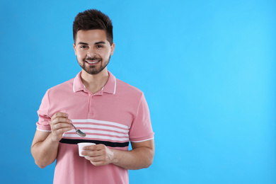 Photo of Happy young man with yogurt and spoon on light blue background. Space for text