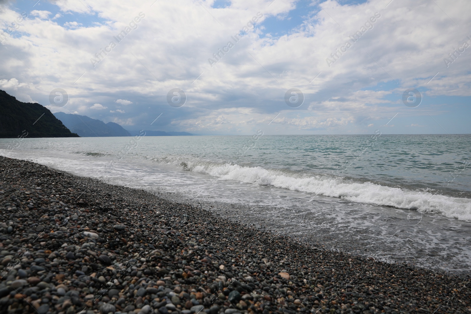 Photo of Picturesque view of beautiful sea shore and mountains under sky with fluffy clouds