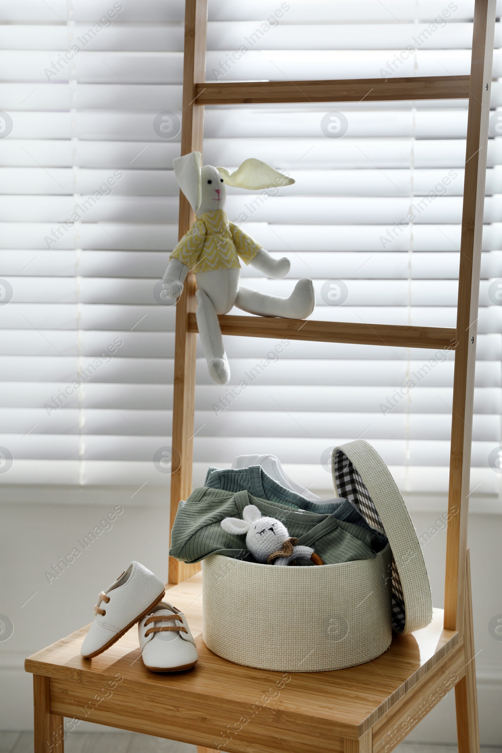 Photo of Box with baby bodysuits, booties and toy on chair indoors