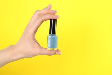 Photo of Woman holding nail polish on yellow background, closeup. Space for text