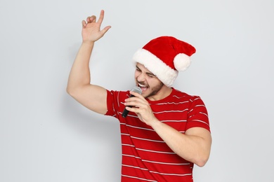 Young man in Santa hat singing into microphone on color background. Christmas music