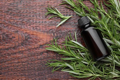 Photo of Bottle of rosemary essential oil on wooden table, flat lay. Space for text