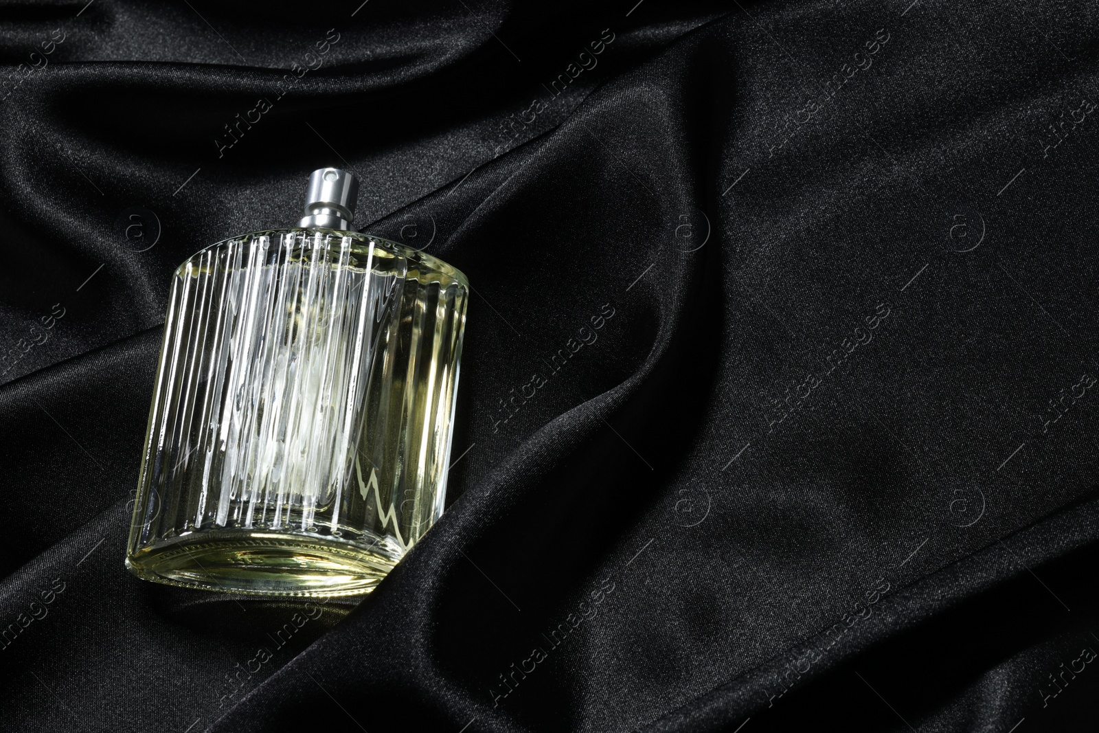 Photo of Luxury men's perfume in bottle on black satin fabric, above view. Space for text