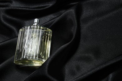 Luxury men's perfume in bottle on black satin fabric, above view. Space for text