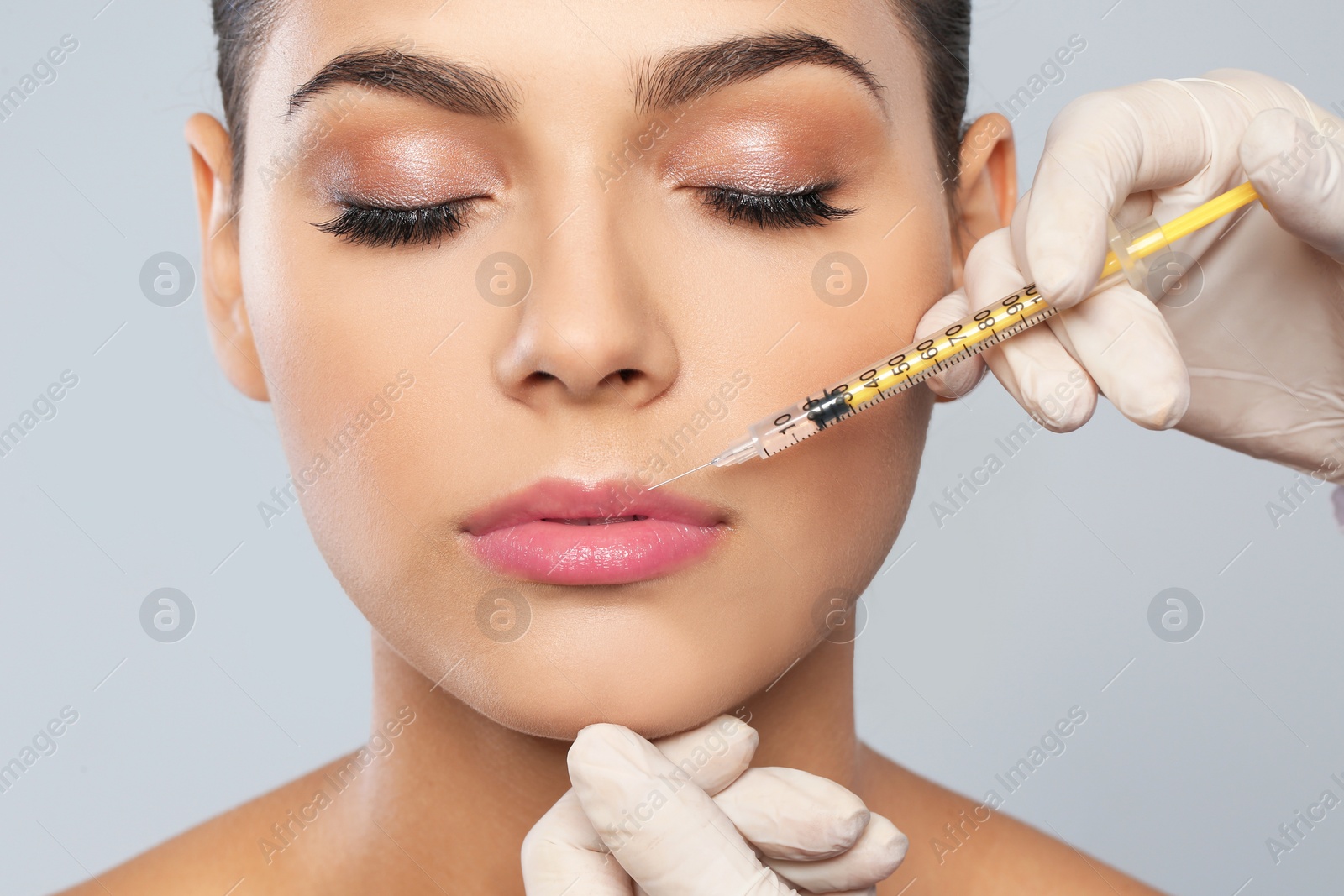 Photo of Young woman getting lips injection on grey background, closeup. Cosmetic surgery