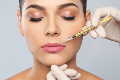 Young woman getting lips injection on grey background, closeup. Cosmetic surgery