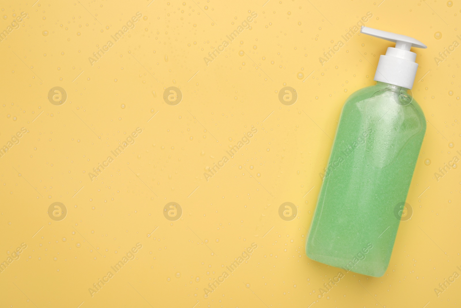 Photo of Wet bottle of face cleansing product on pale orange background, top view. Space for text
