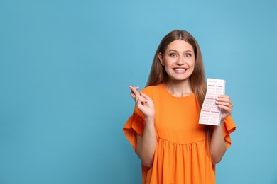 Photo of Portrait of hopeful young woman with lottery ticket on light blue background, space for text