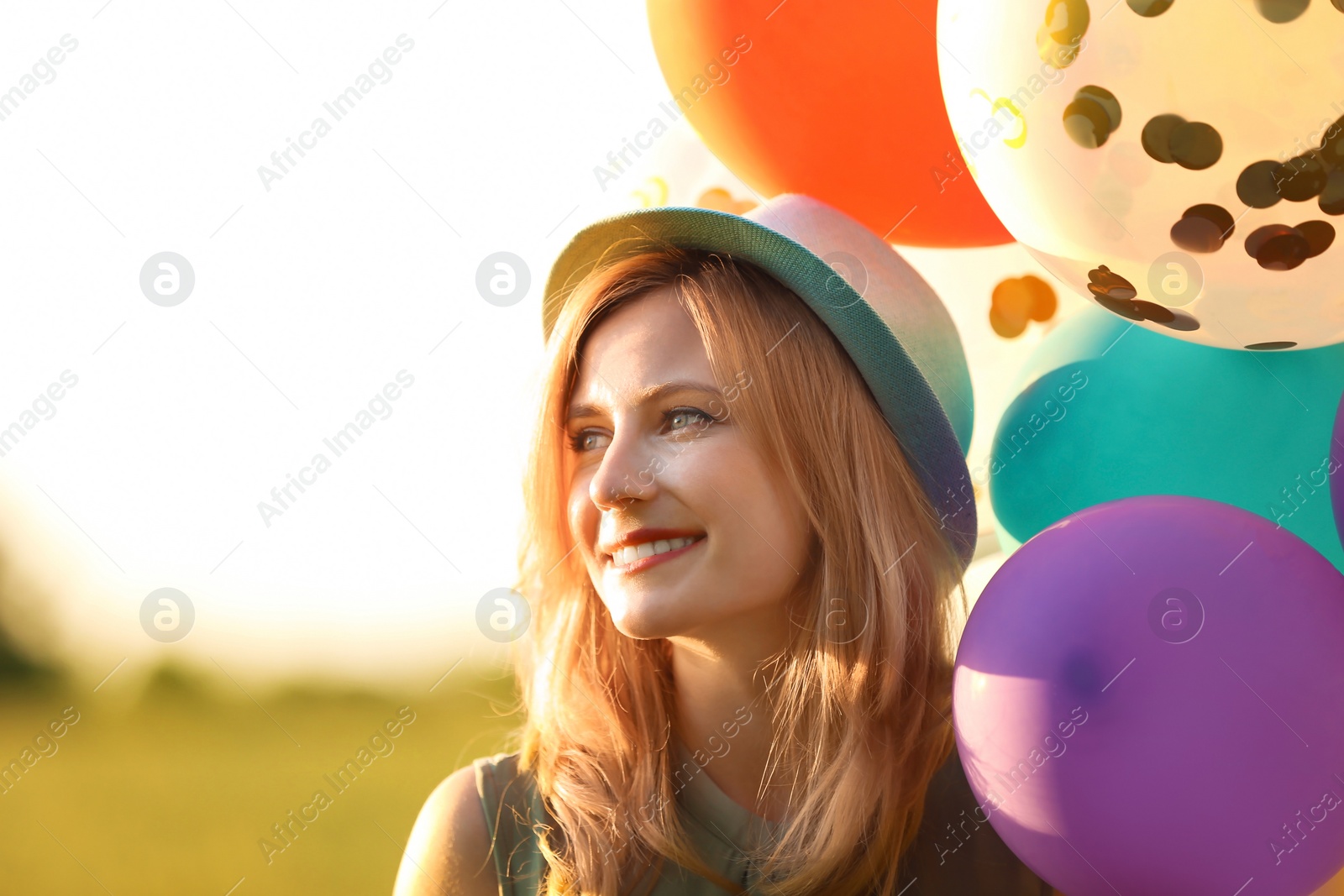 Photo of Young woman with colorful balloons outdoors on sunny day