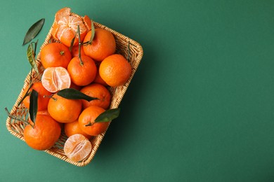 Fresh ripe tangerines with leaves in wicker basket on green background, top view. Space for text