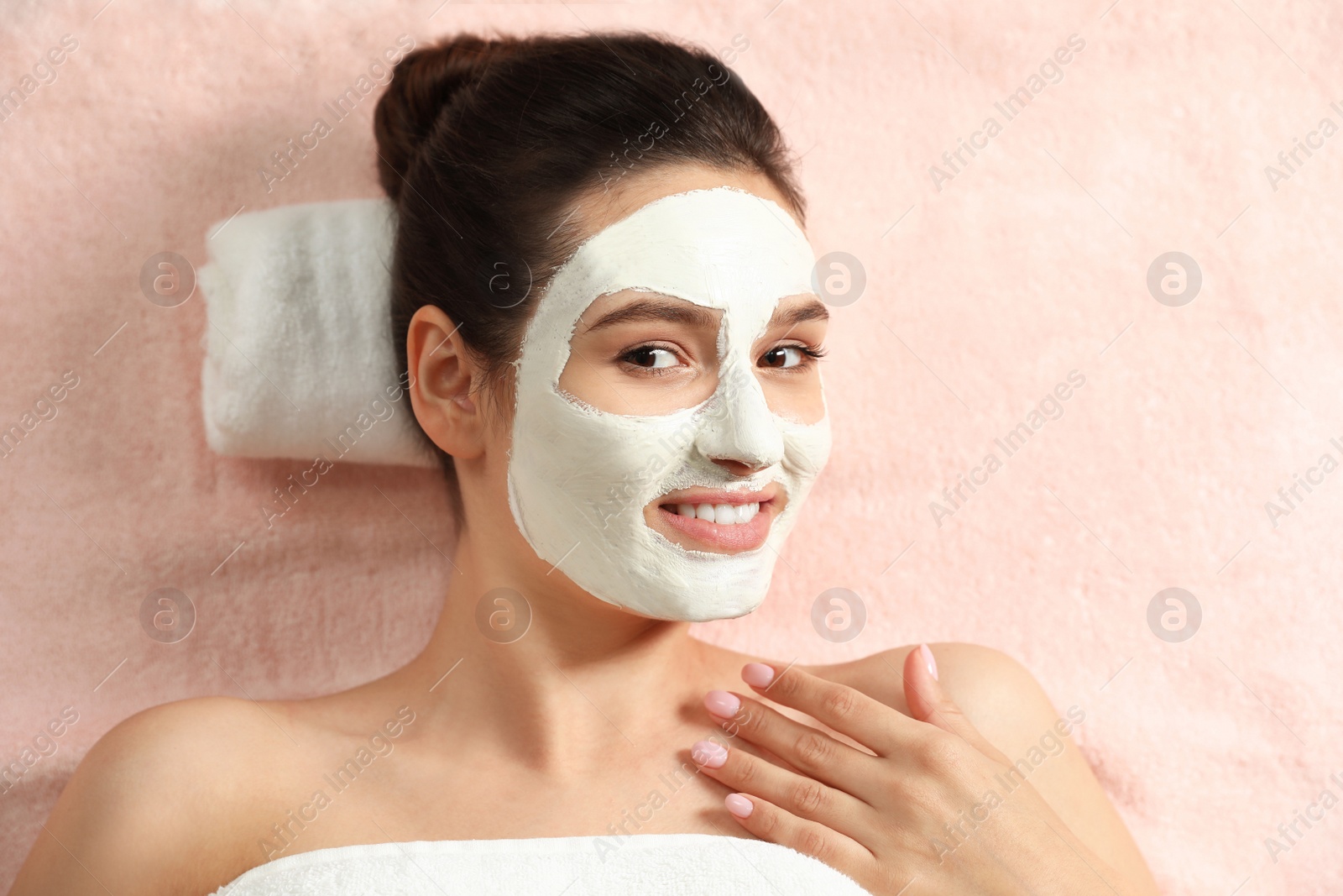 Photo of Beautiful woman with white mask on face relaxing in spa salon, top view