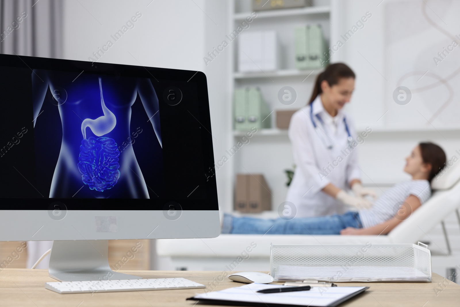 Photo of Gastroenterologist examining girl in clinic, focus on computer with image of digestive tract on table