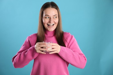 Photo of Happy woman with milk mustache holding glass of drink on light blue background