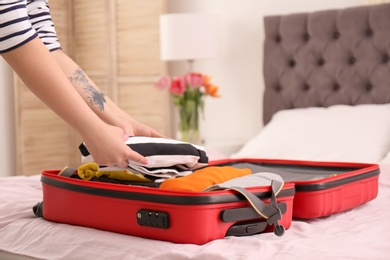 Photo of Young woman packing suitcase on bed