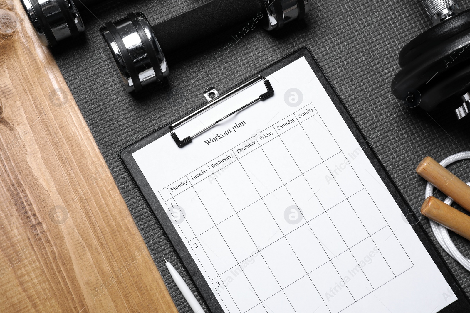 Photo of Clipboard with workout plan and sports equipment on wooden table, flat lay. Personal training