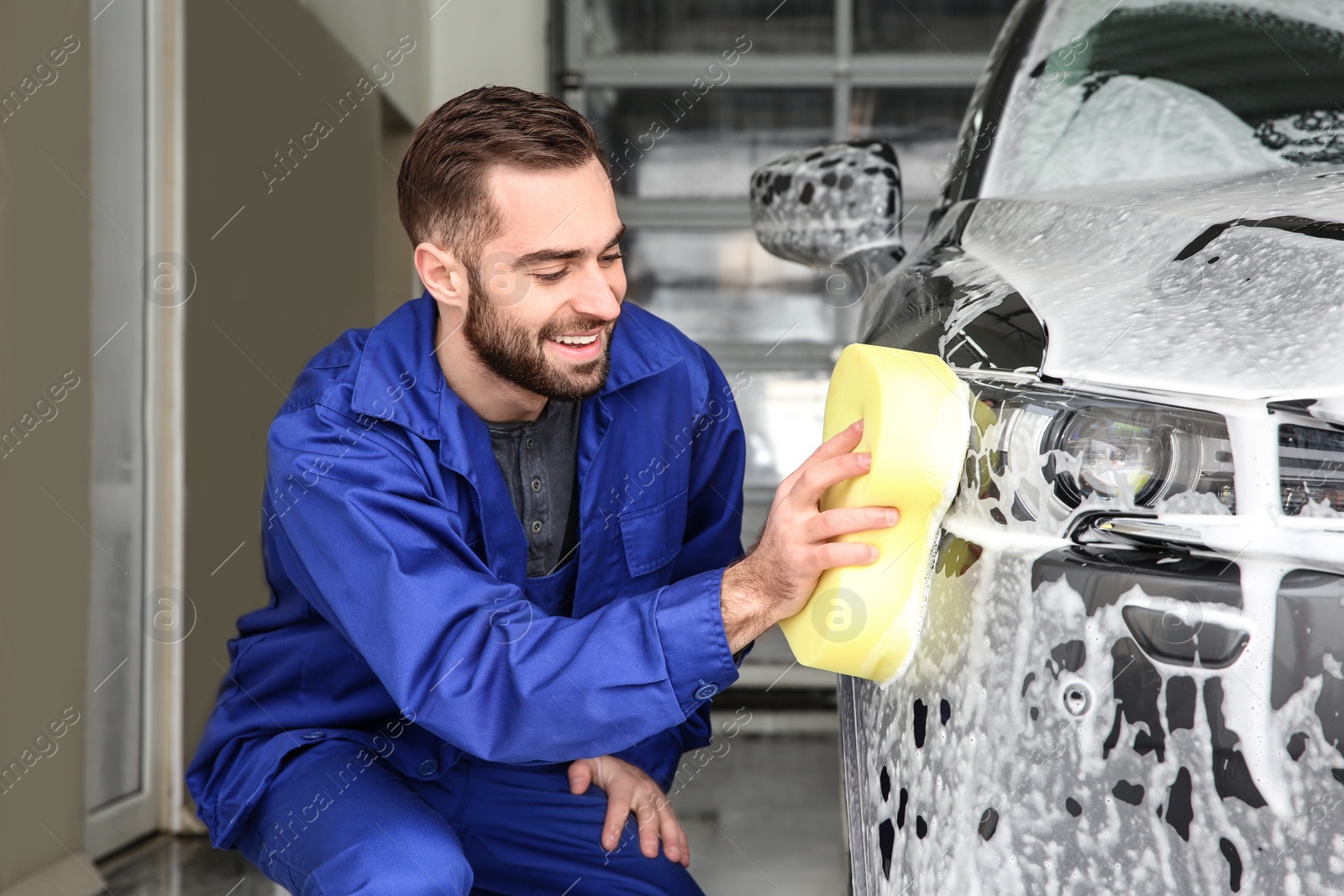 Photo of Worker cleaning automobile with sponge at professional car wash