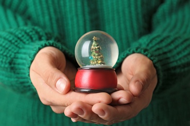 Photo of Woman wearing green sweater holding snow globe with Christmas tree, closeup