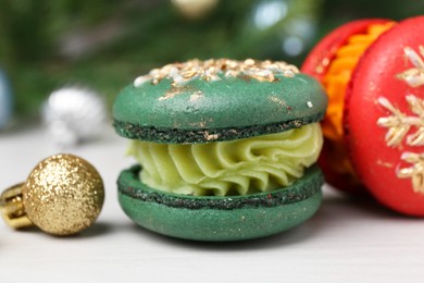 Different decorated Christmas macarons and festive decor on white table, closeup