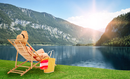 Young woman relaxing on sun lounger near river and mountains. Luxury vacation 