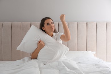 Angry young woman suffering from noisy neighbours in bed at home