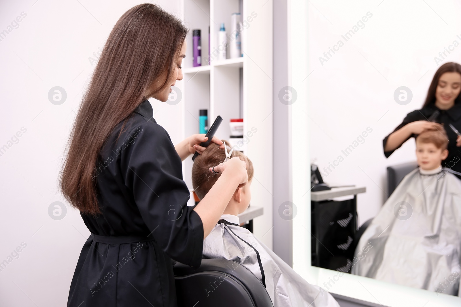 Photo of Professional female hairdresser working with little boy in salon